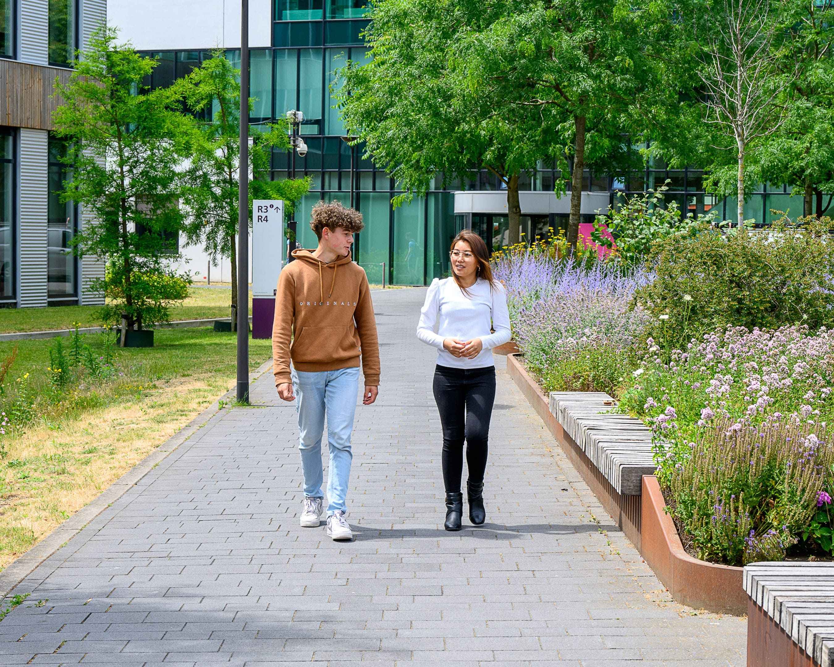 Twee studenten pratend en lopend buiten op de campus voor de opleiding Ondernemerschap & Retail Management.