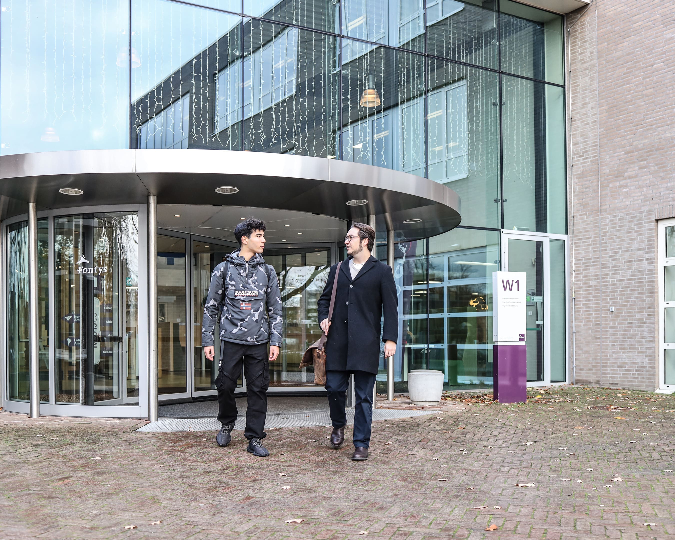 Two students walking and talking outside the entrance of the campus.