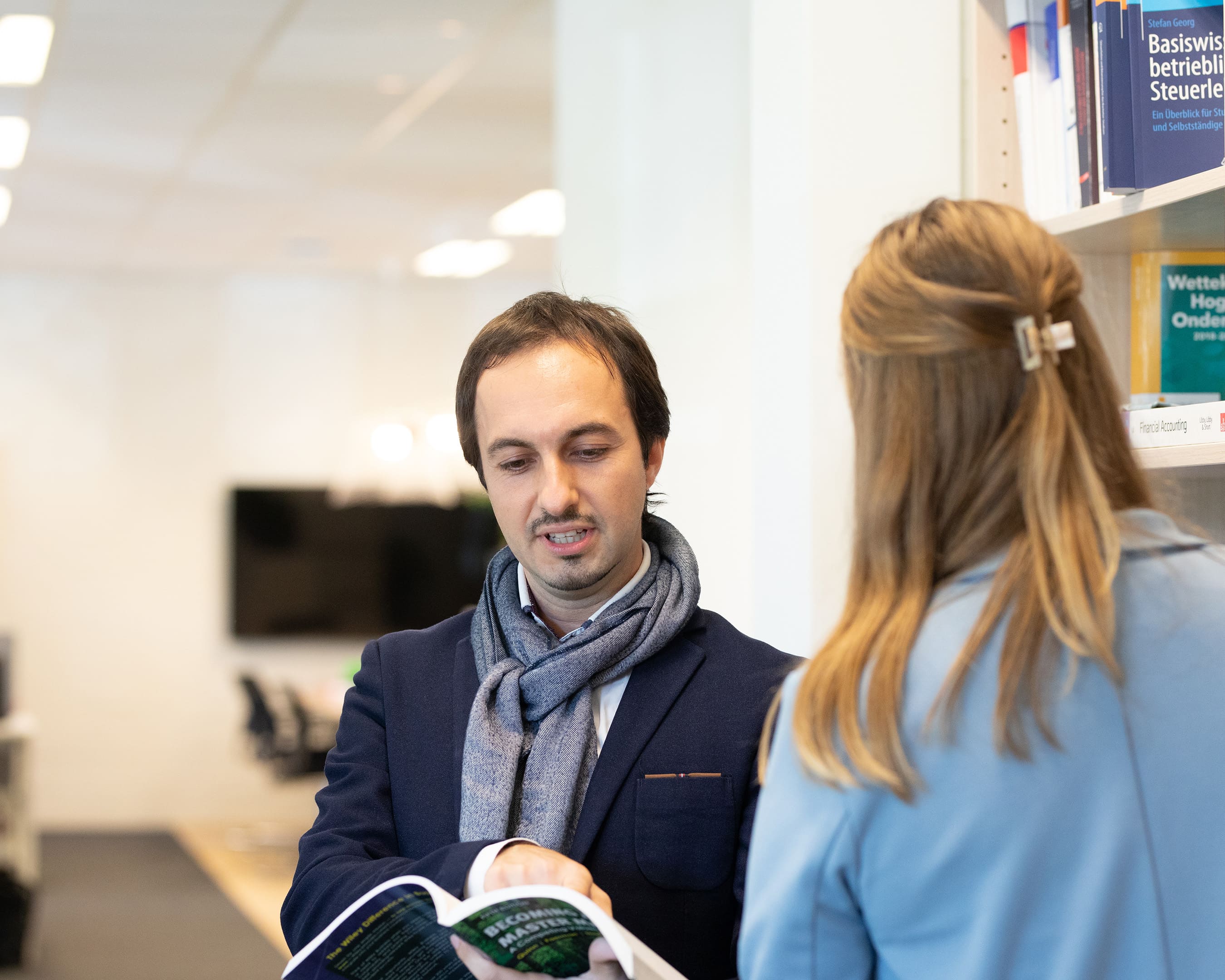 Two students discussing a book in a library.