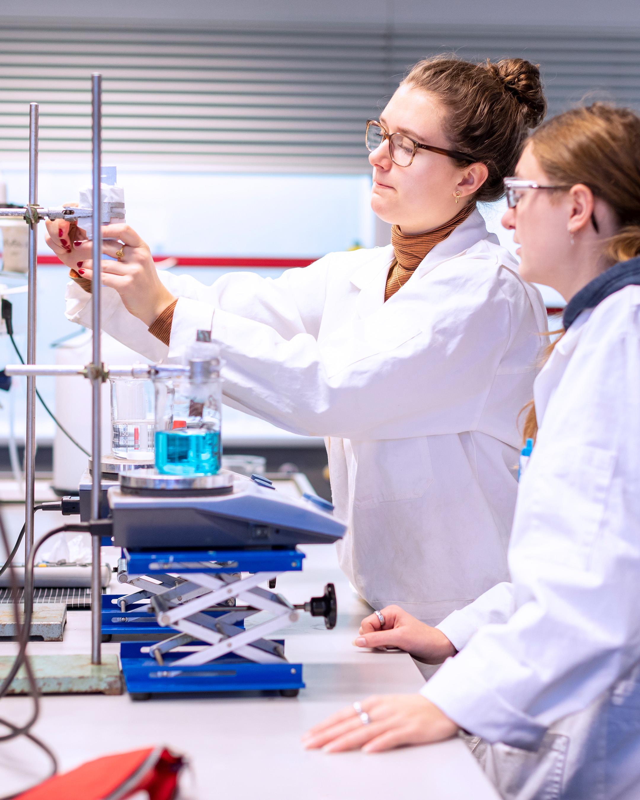 Student met witte jas staat achter een tafel voor opleiding Leraar Scheikunde