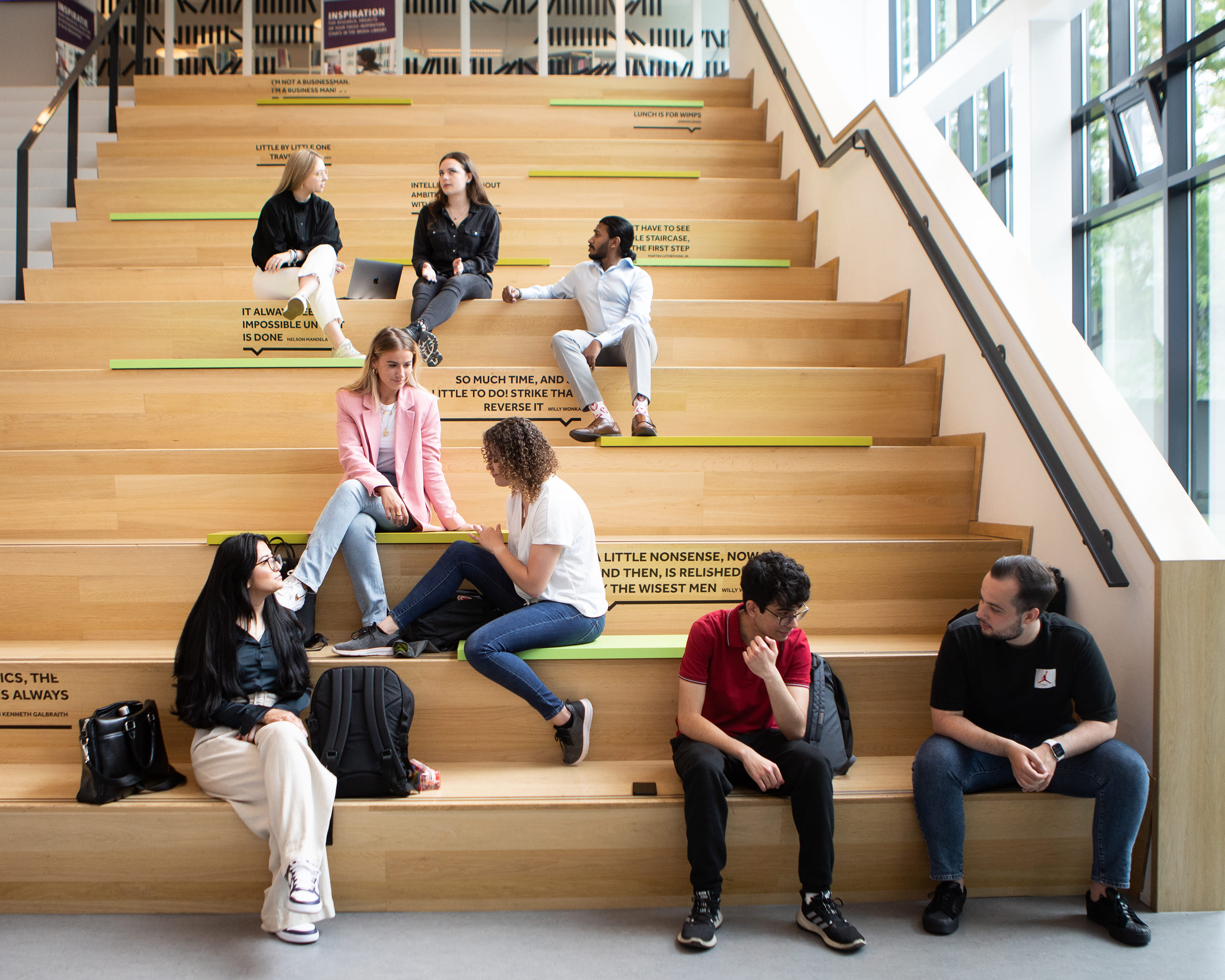 Studenten van de opleiding Ondernemerschap & Retail Management zitten op de trap in het gebouw.