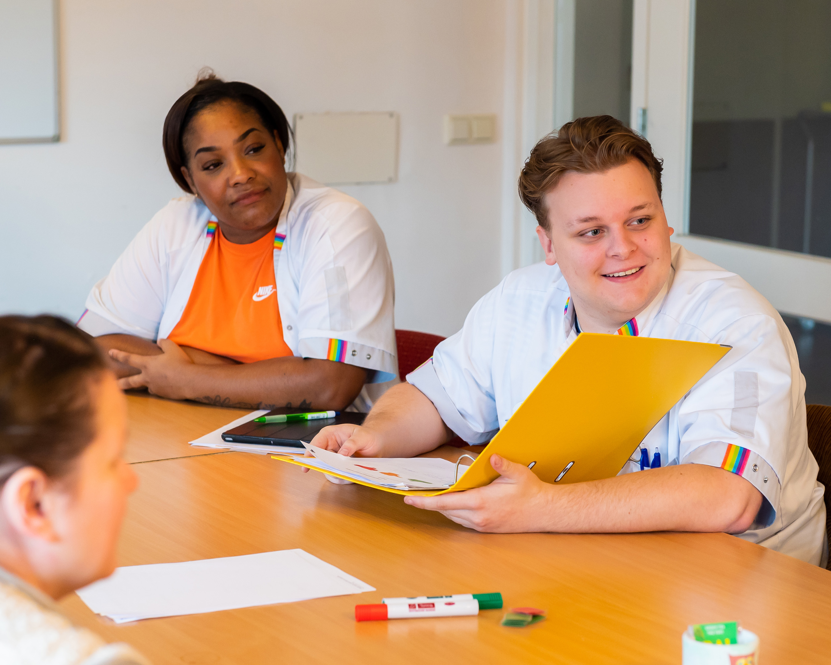 Studenten van de opleiding Verpleegkunde in een werksituatie aan een tafel met een dossier.