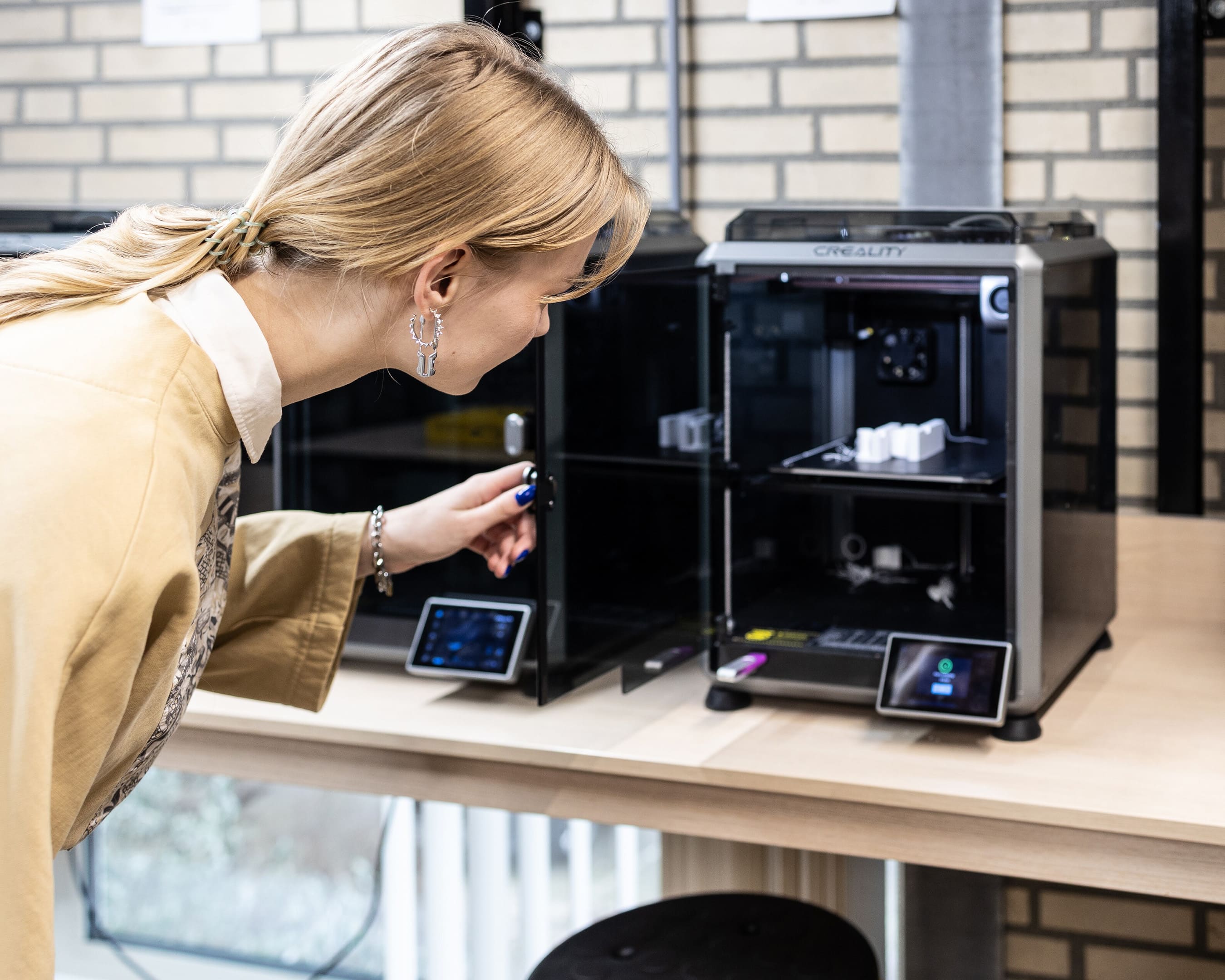 A IDE student operating a 3D printer in a workshop, inspecting the printing process.