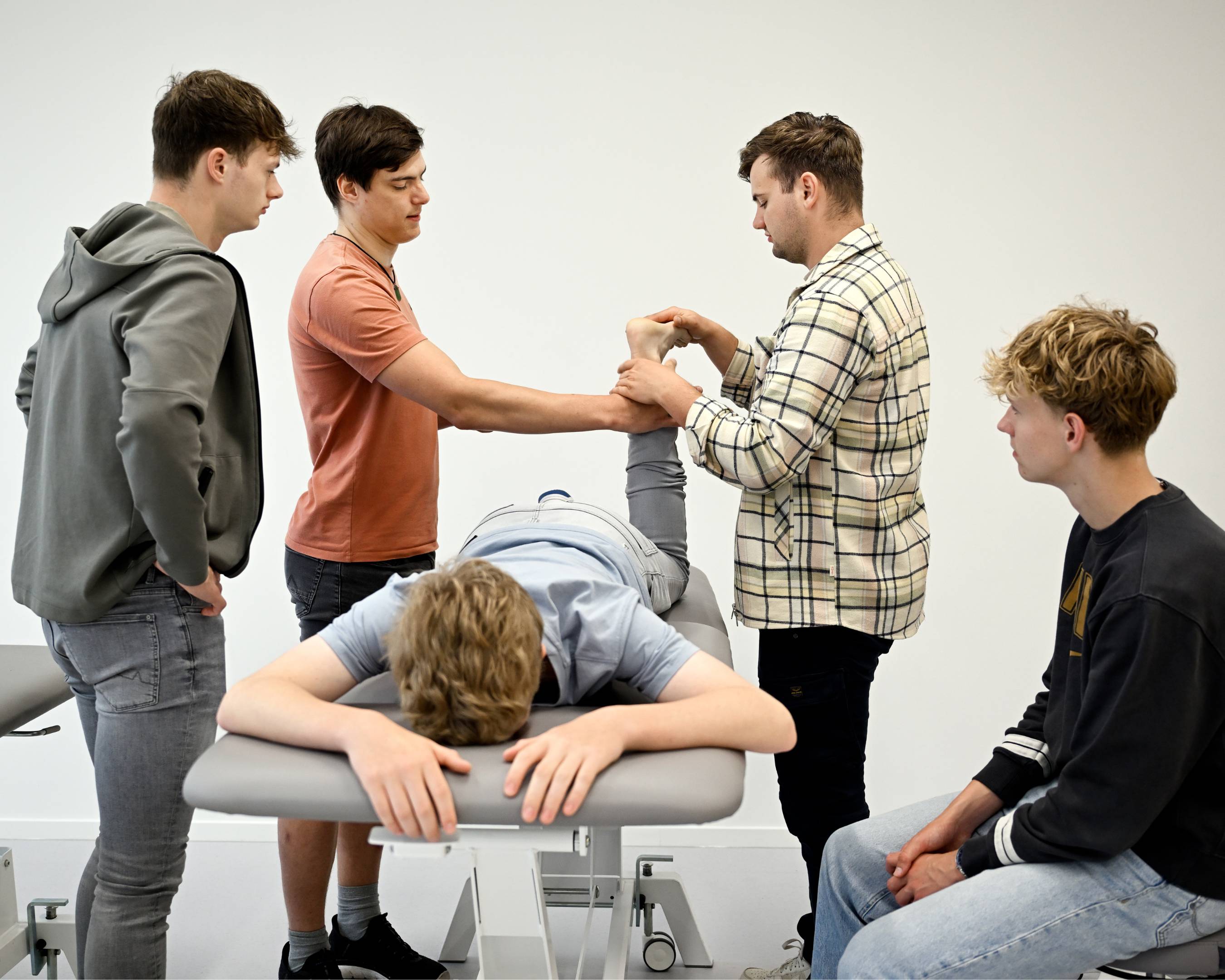 Fysiotherapiestudenten oefenen een behandeling op een medestudent die op een behandeltafel ligt.