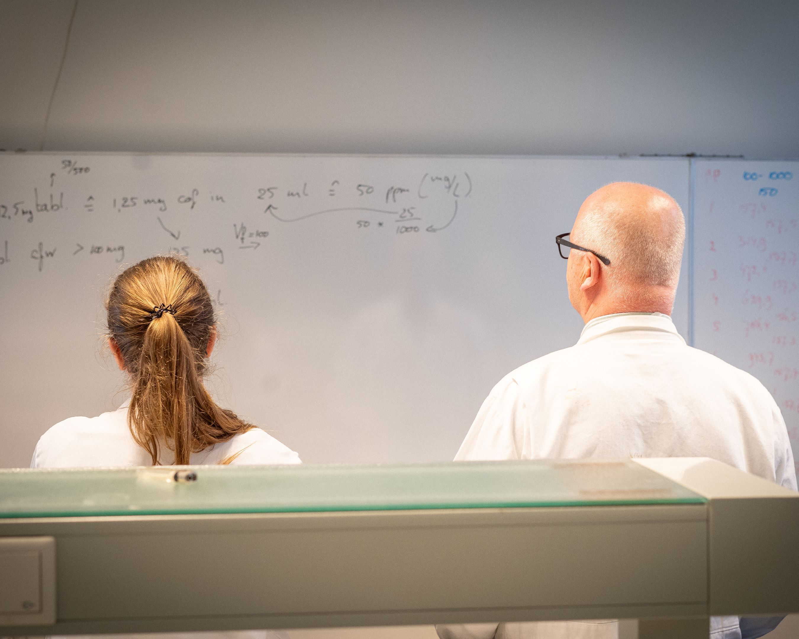 Docent en student kijken naar whiteboard voor Leraar Scheikunde