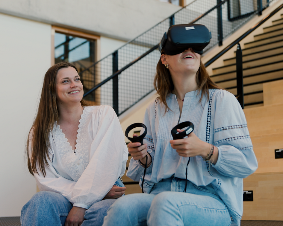 Twee studenten zitten op een trap, één gebruikt een VR-headset met controllers