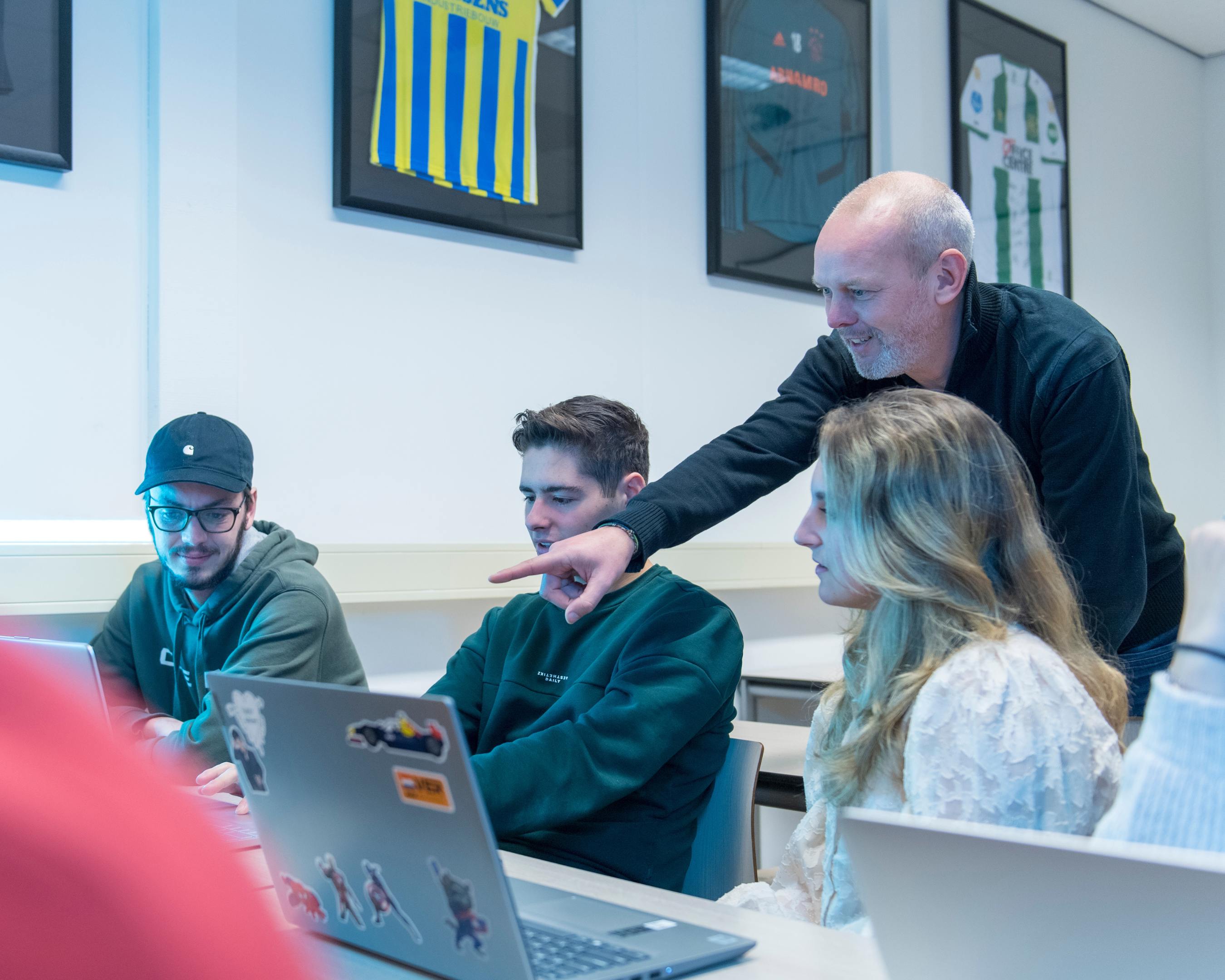 Een docent wijst naar laptop bij drie studenten