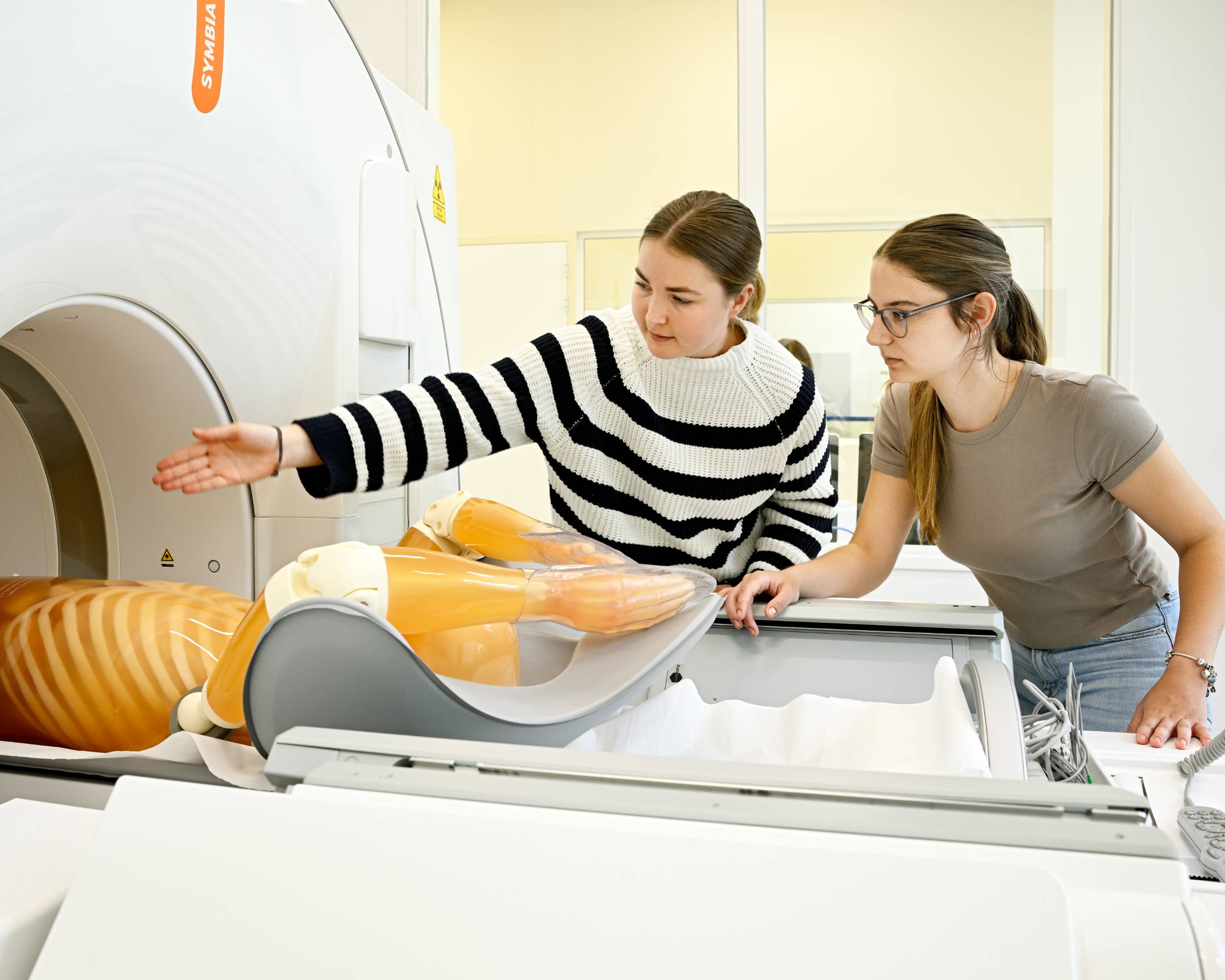 Twee studenten bij een MRI-scanner bespreken de positie van een anatomisch model.