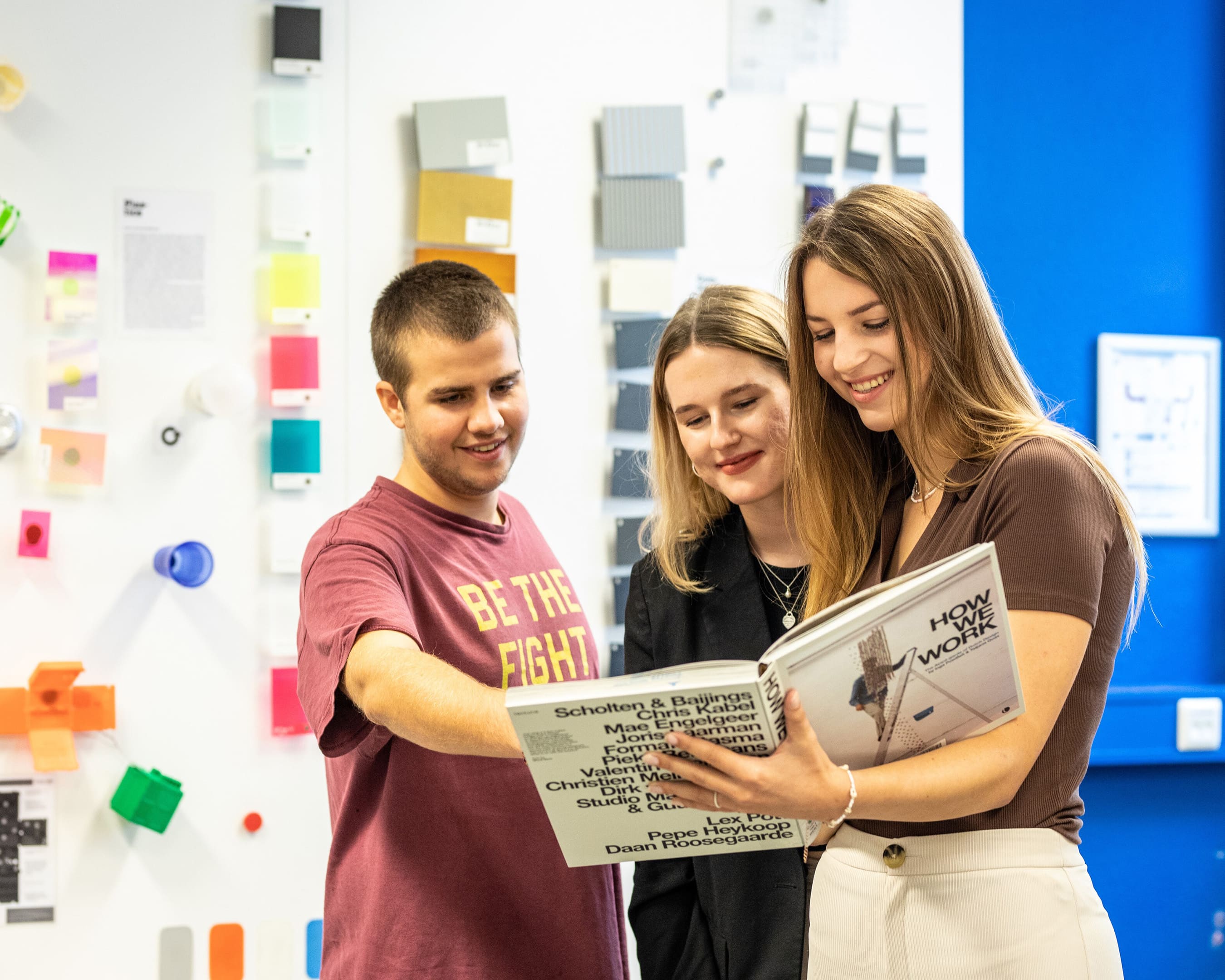 Industrial Design Engineering students viewing a design book with samples in the background.