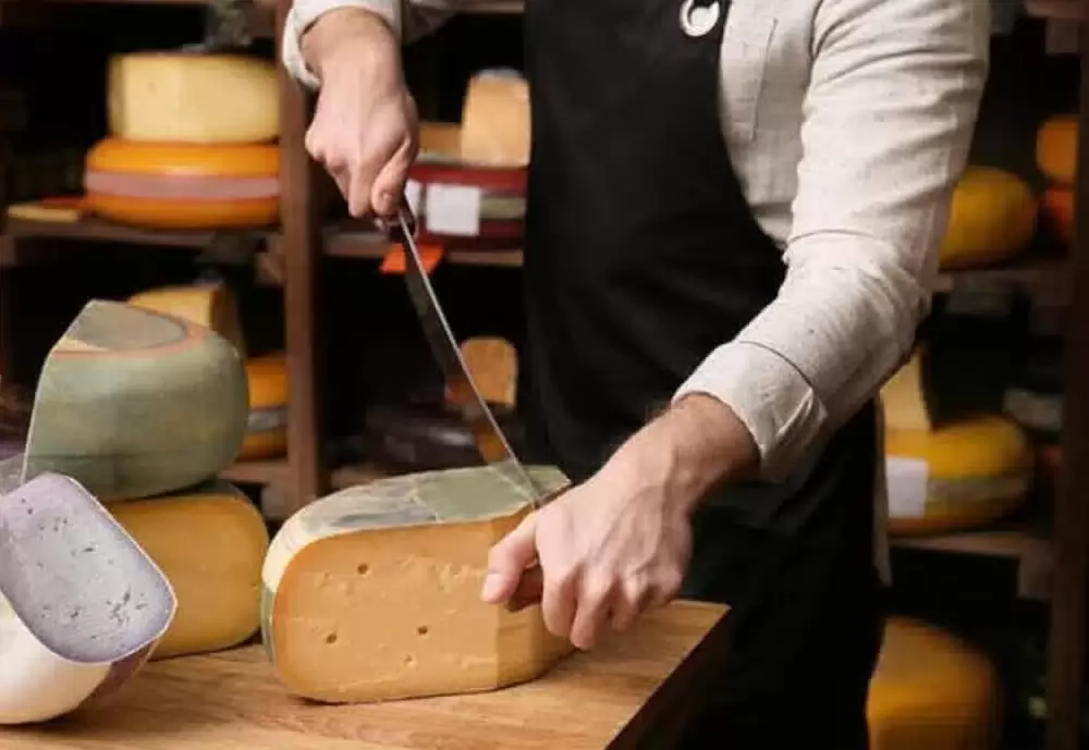 Image of a person cutting a slice of Dutch cheese.