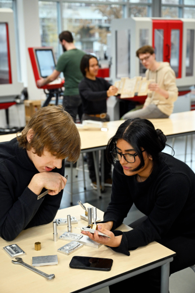 Studenten Werktuigbouwkunde werken samen aan technische onderdelen aan een tafel.