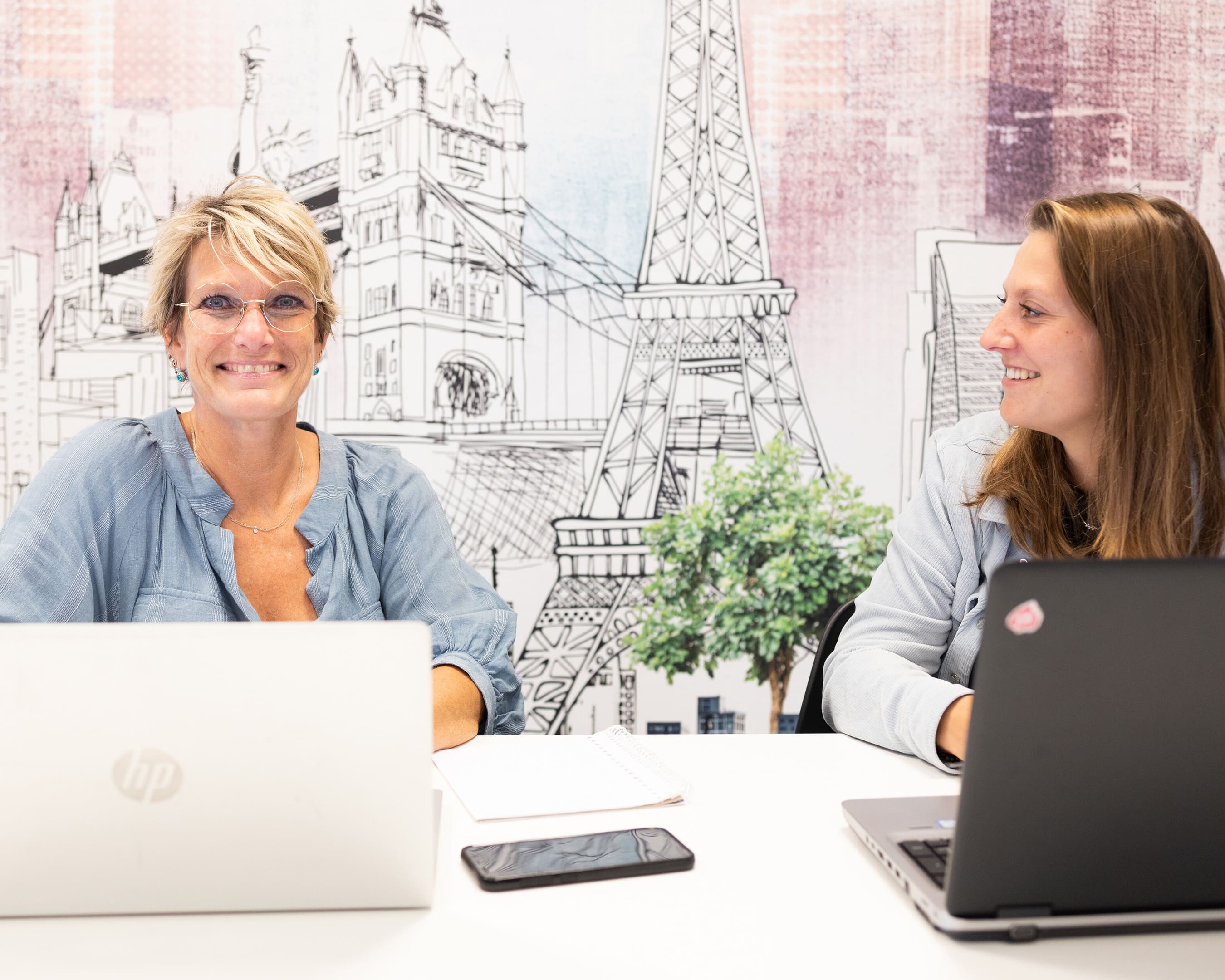 Two students smile at each other while working together on laptops