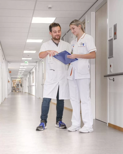 Twee verpleegkundestudenten in uniform bekijken samen een dossier.