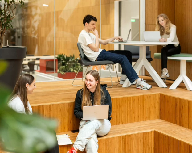 Studenten van de opleidng Social Work zitten in een ontspannen werkhouding op de trap en aan een tafel.