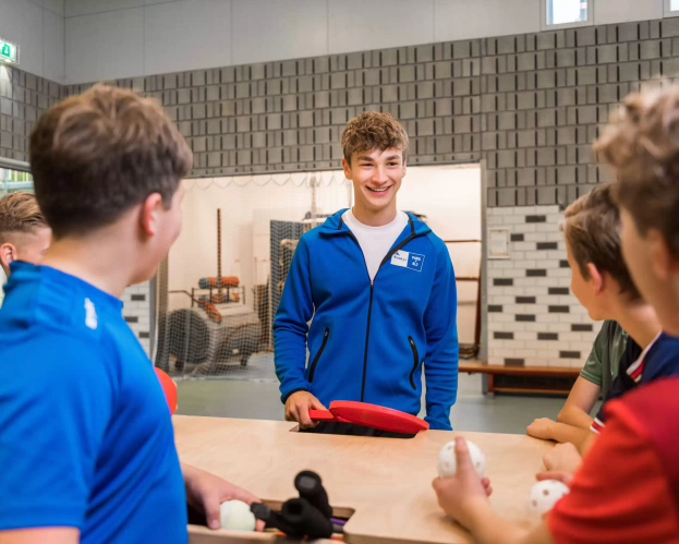 Studenten in sportkleren in een sportzaal kijken naar een tablet waarop instructies staan.