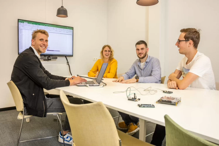 Studenten werken samen met docent aan technische projecten in een werkruimte, met gereedschap en elektronica op de tafel.