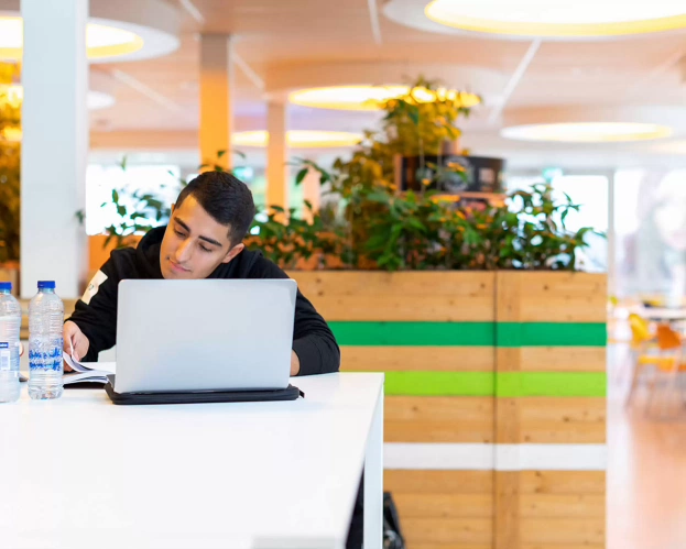 Student achter een laptop aan tafel.