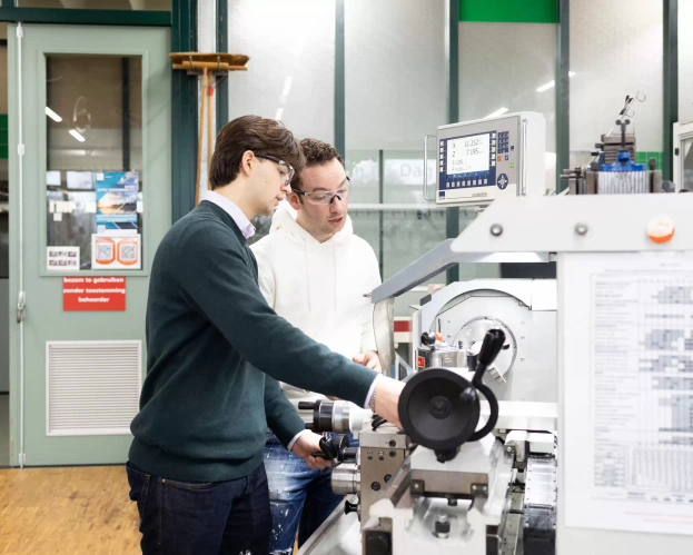 Twee studenten Ad Engineering werken samen aan een machine in een technische werkplaats.