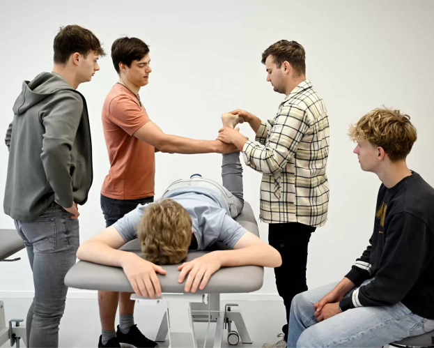 Fysiotherapiestudenten oefenen een behandeling op een medestudent die op een behandeltafel ligt.