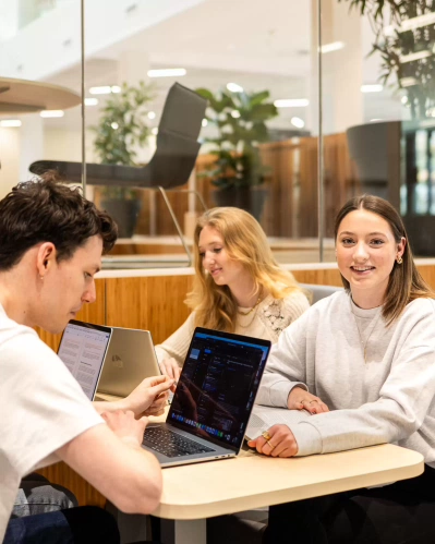 Drie studenten van de opleiding Social Work aan een tafel met labtops, ze zijn bezig met projectwerk.