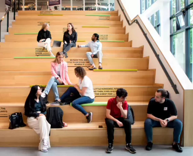 Studenten van de opleiding Ondernemerschap & Retail Management zitten op de trap in het gebouw.